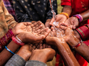 Photo of a group of people's hands with water pouring over them.